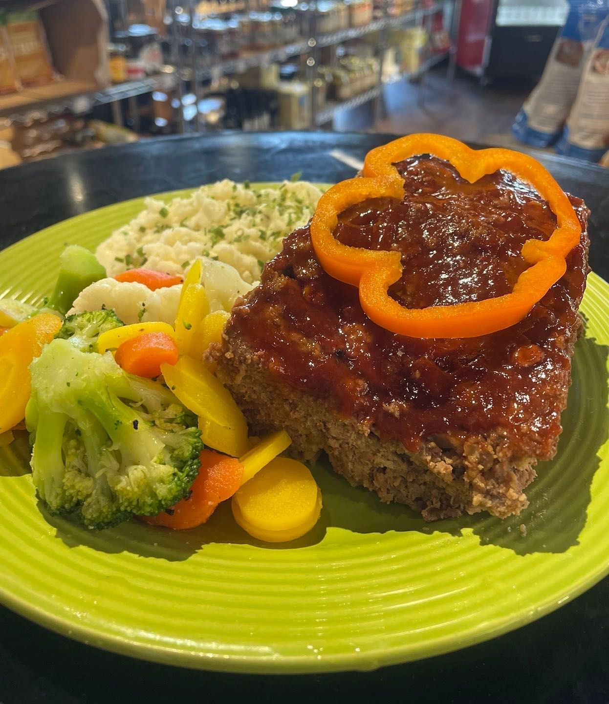 Meatloaf topped with pepper ring, served with vegetables and mashed potatoes