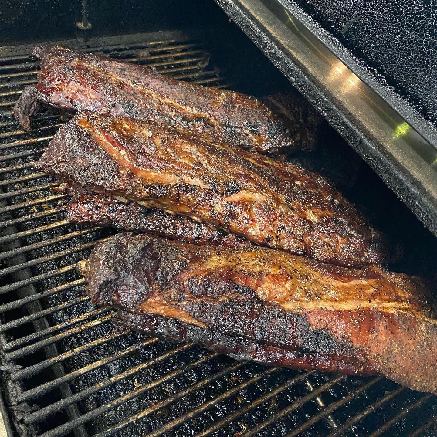 Smoked meat on a grill, with a dark, seasoned exterior