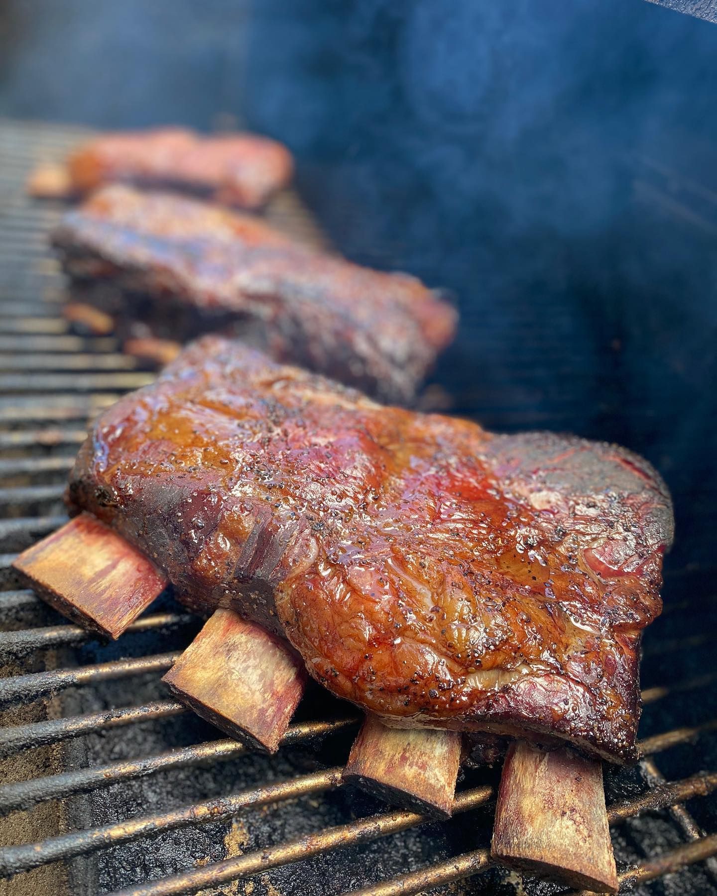 Smoked beef short ribs on a grill with smoke rising