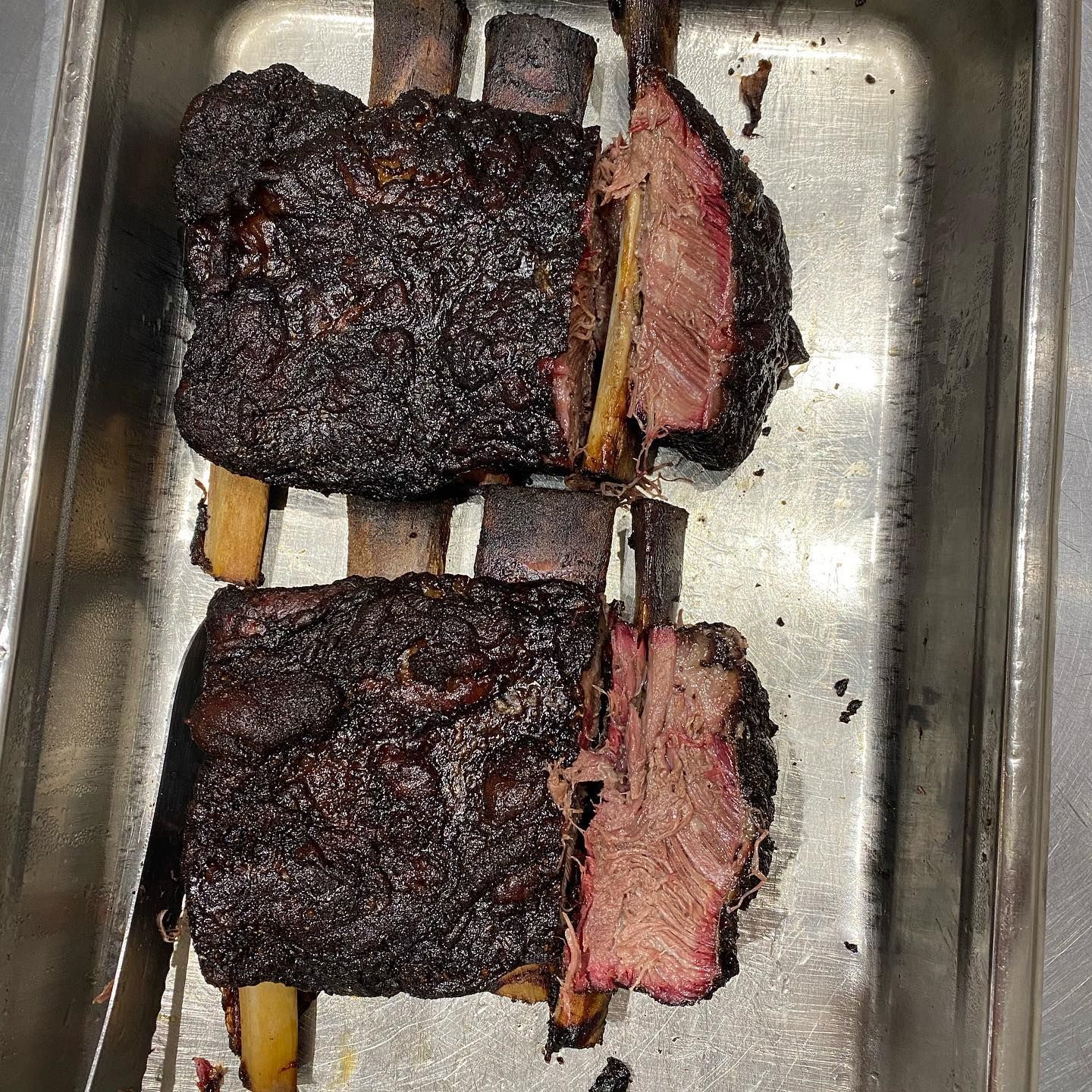 Smoked beef short ribs, cut to reveal juicy, pink meat, resting in a metal pan