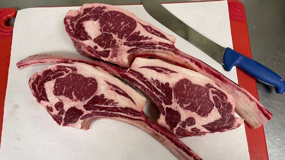 Two raw tomahawk steaks with a knife on a cutting board