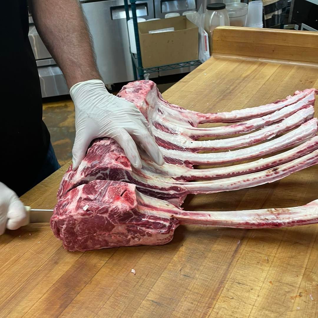 A person cutting a large raw tomahawk steak with a knife on a wooden butcher block