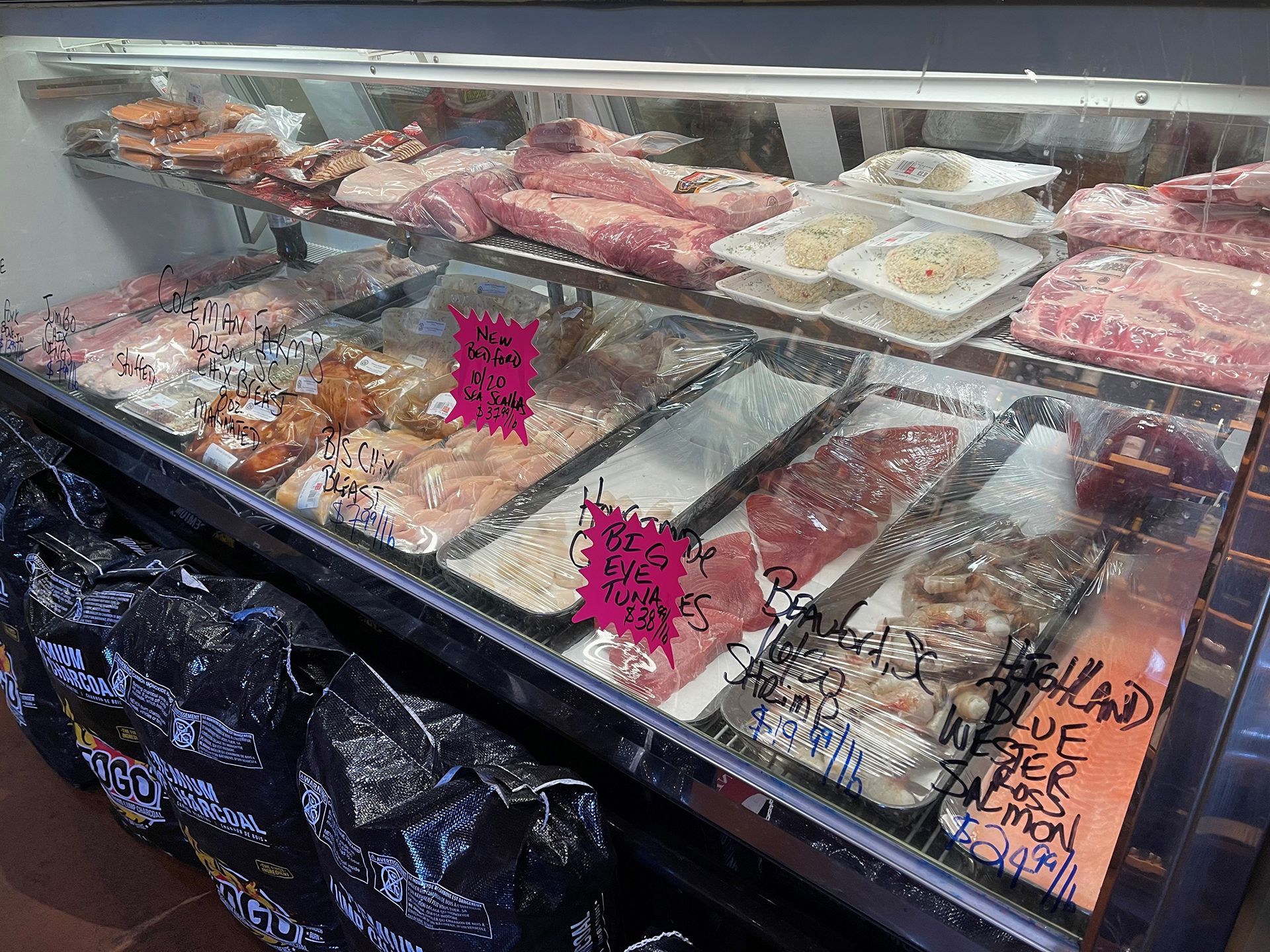 A refrigerated display case filled with various cuts of raw meat at a butcher shop