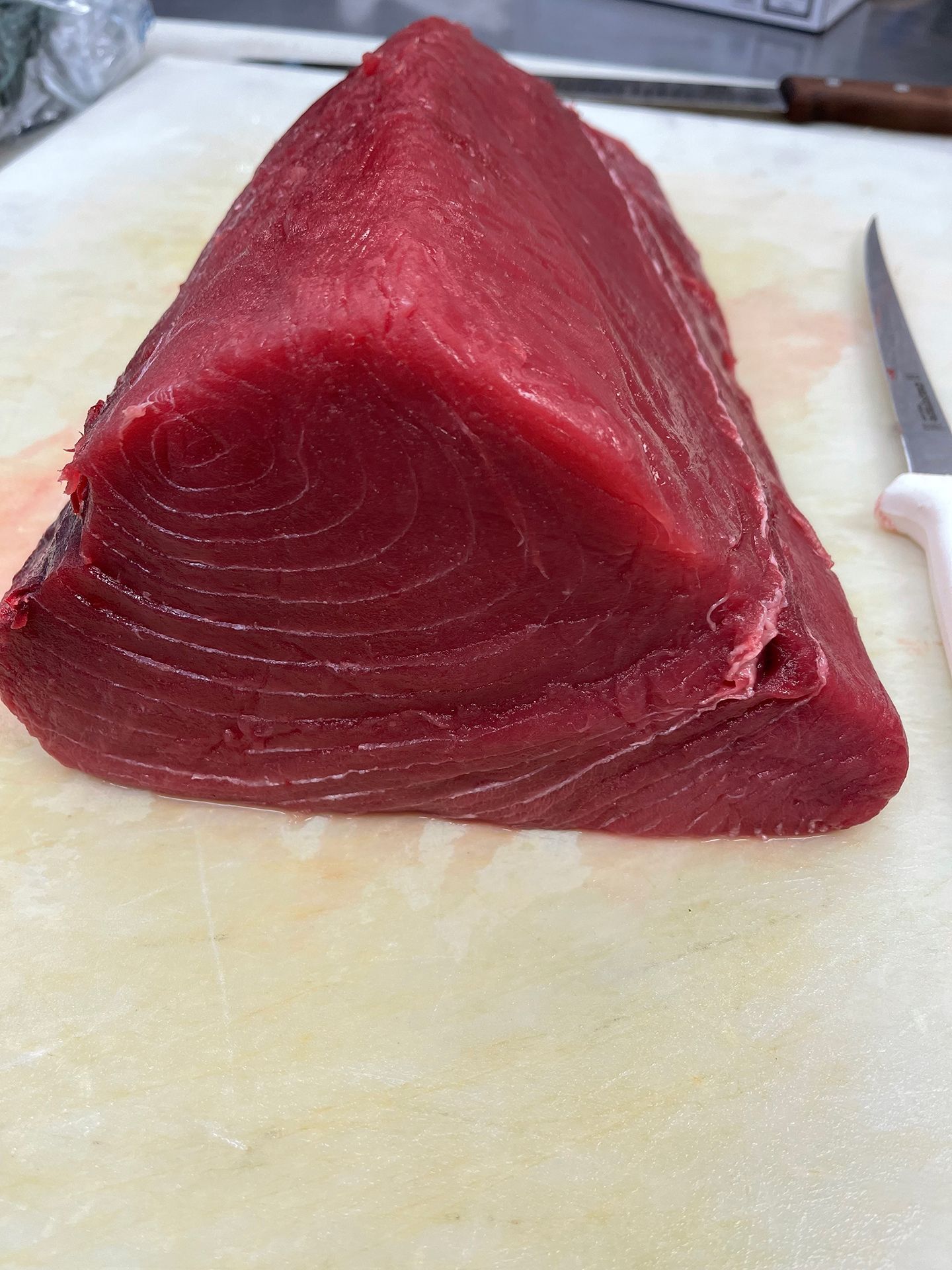 Raw bluefin tuna steak on a white cutting board next to a knife