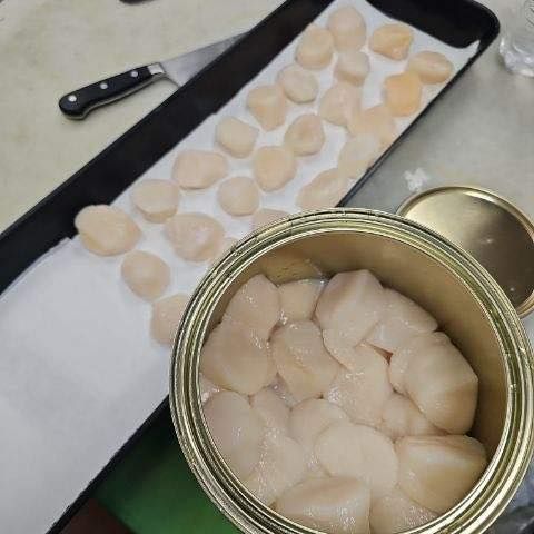 Scallops from a can, spread on a tray with a knife beside it