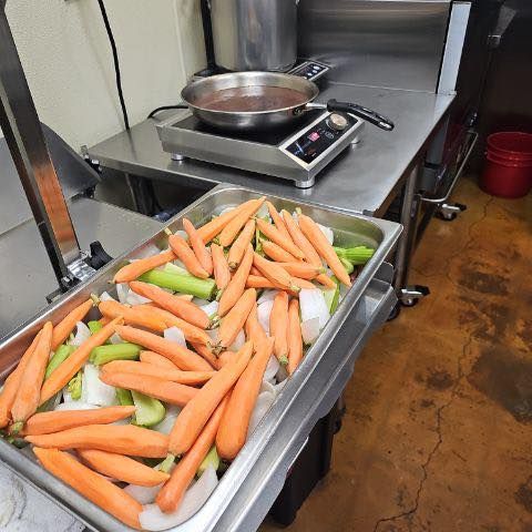 Tray of carrots and celery next to a hot plate with a pan on top in a kitchen setting