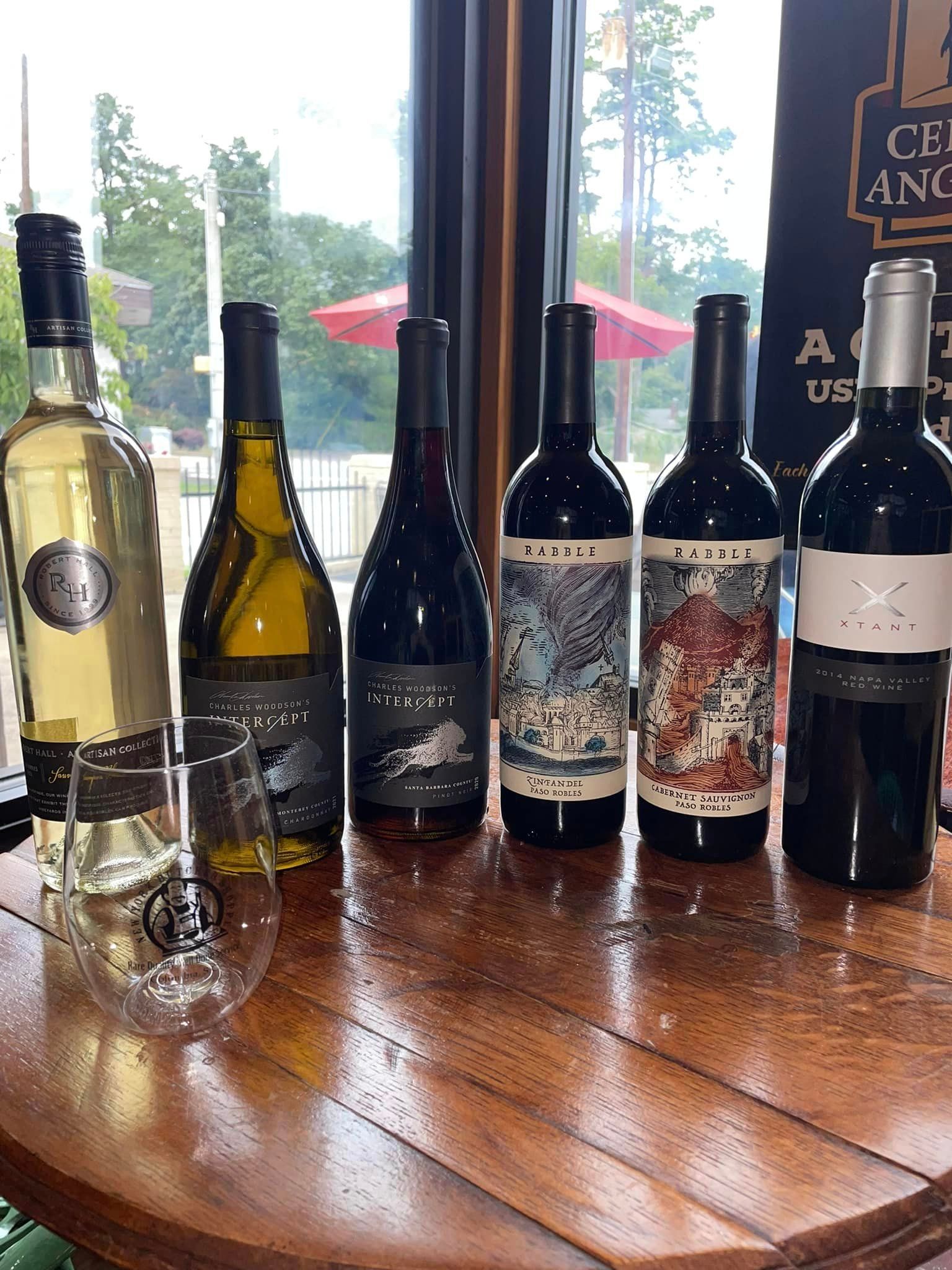 Six wine bottles and a glass on a wooden table
