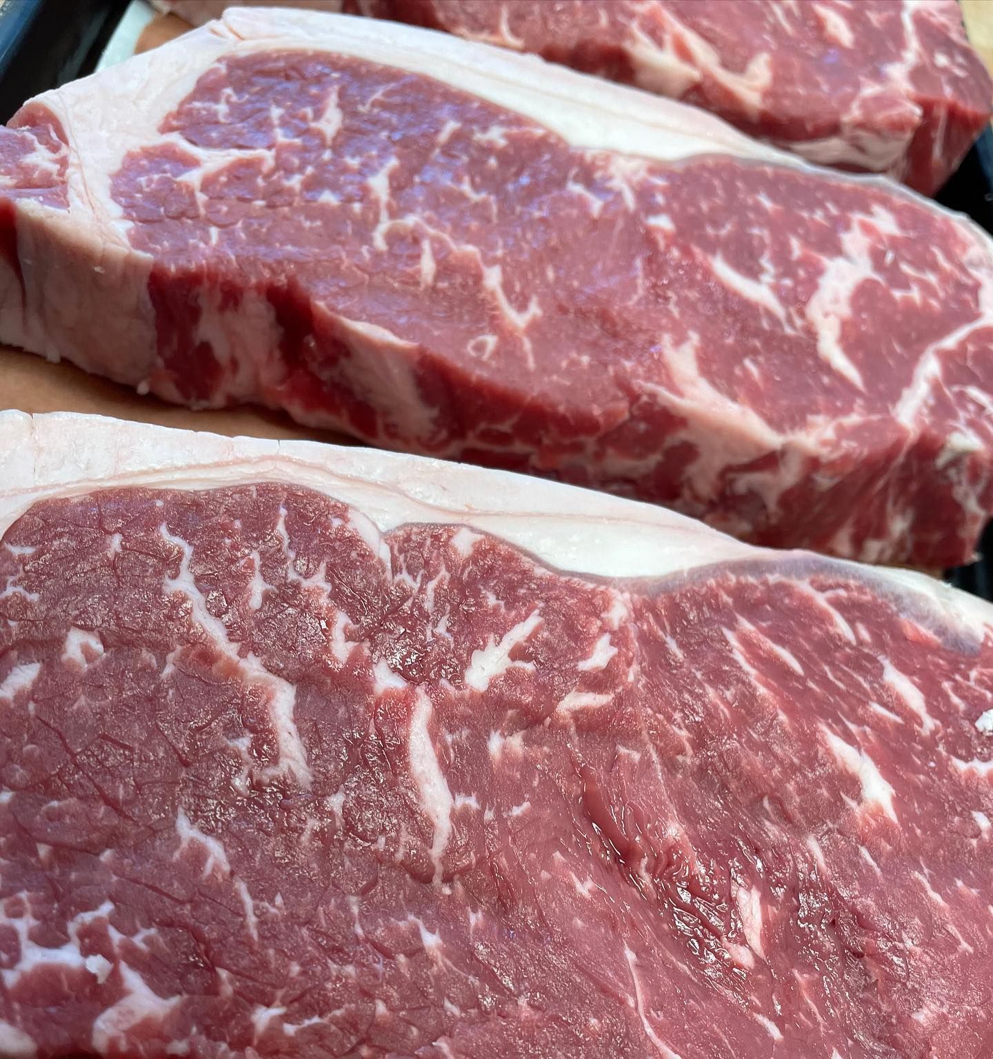 Close-up of three raw New York strip steaks with visible marbling and fat.
