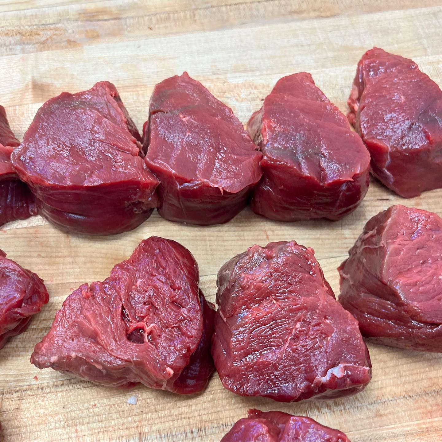 Chunks of red meat on a wooden cutting board.