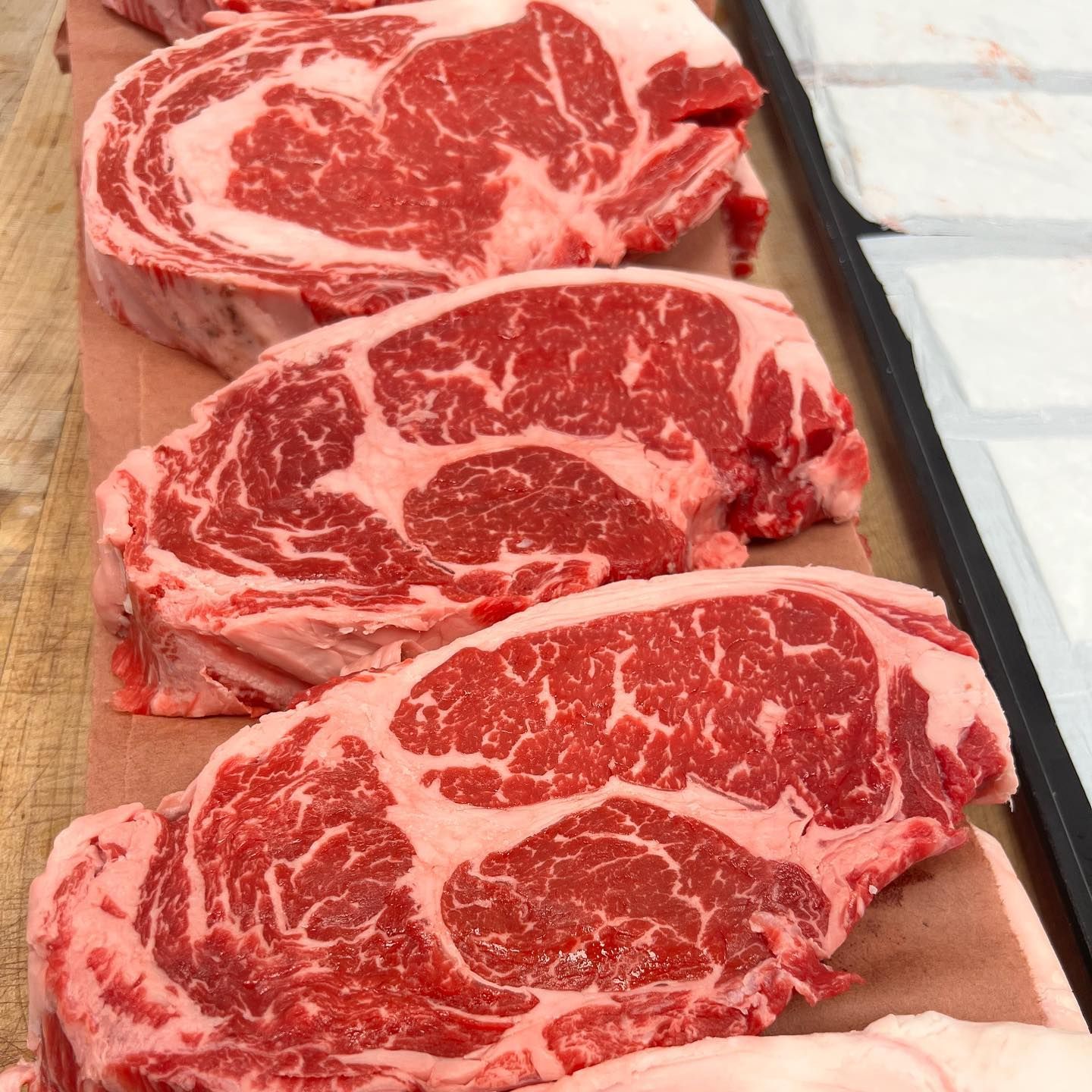 Raw ribeye steaks with marbling, arranged on butcher paper.