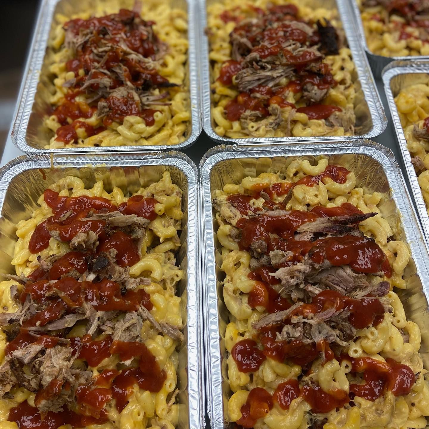 Mac and cheese trays topped with pulled meat and barbecue sauce.