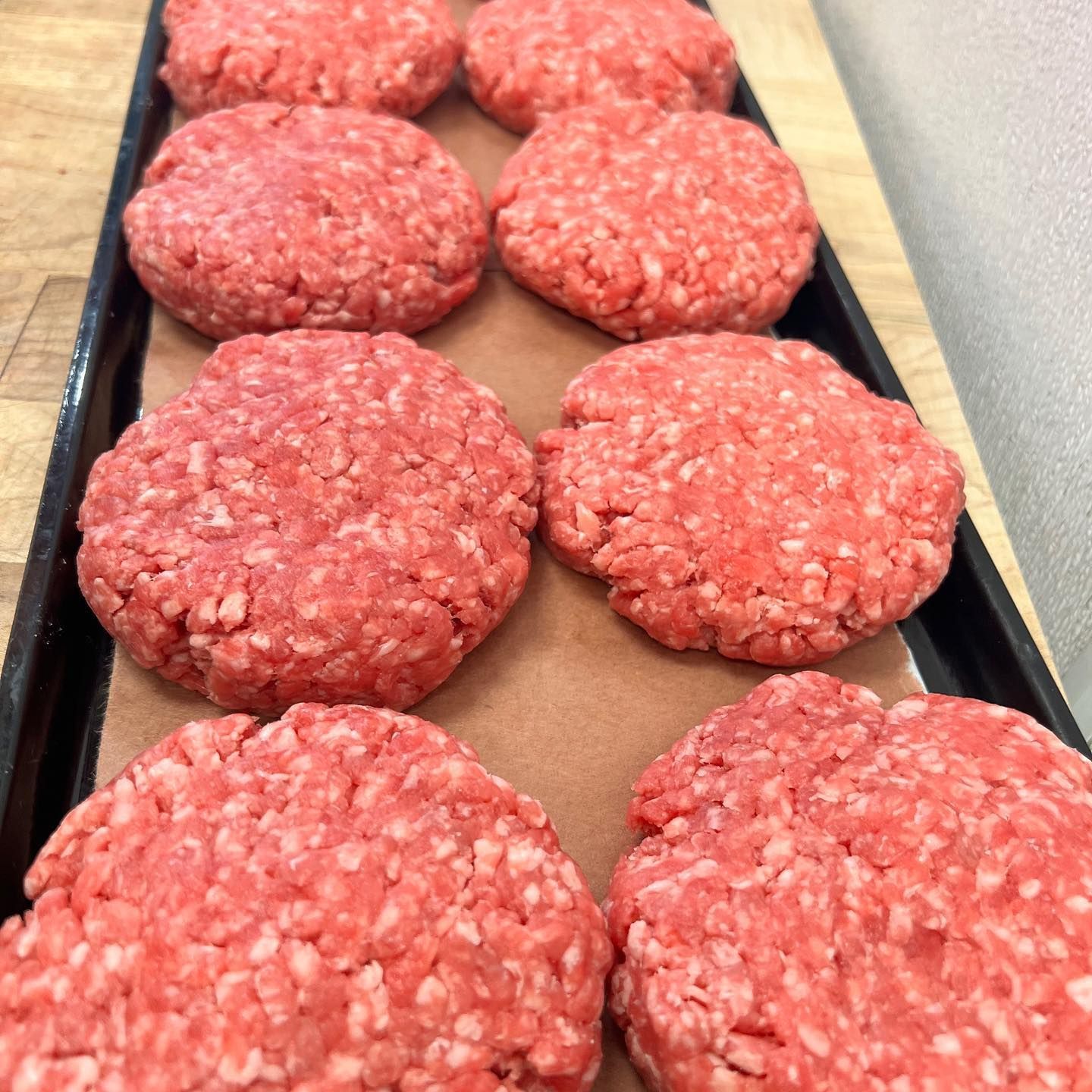 Raw hamburger patties on a brown lined black tray, ready for grilling.