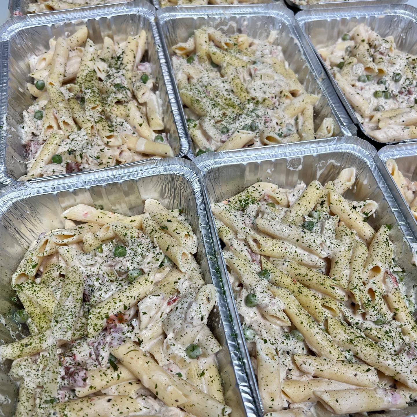 Penne pasta with cream sauce and peas in multiple foil containers, ready for catering.