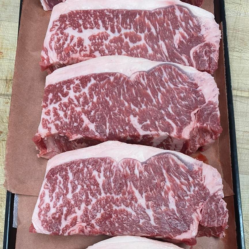 Three raw New York strip steaks with marbled fat displayed on butcher paper.