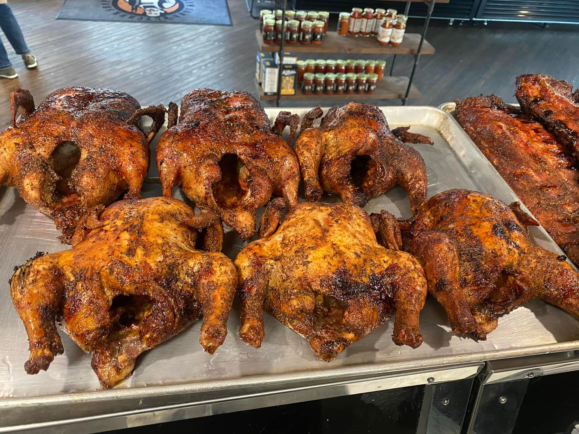 Tray of roasted chickens, golden brown, with a shelf of sauces in the background.