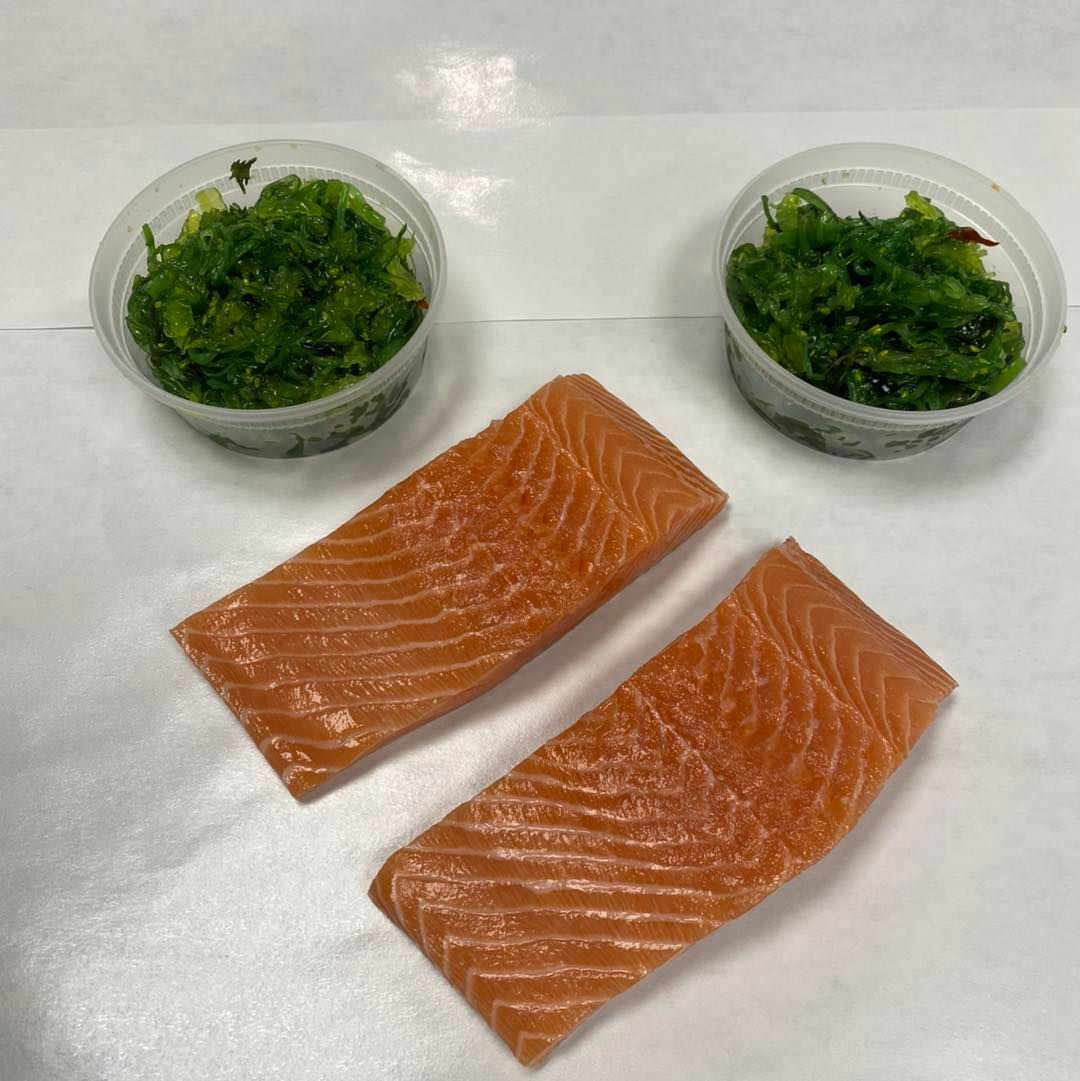 Two salmon fillets and two containers of seaweed salad on white.