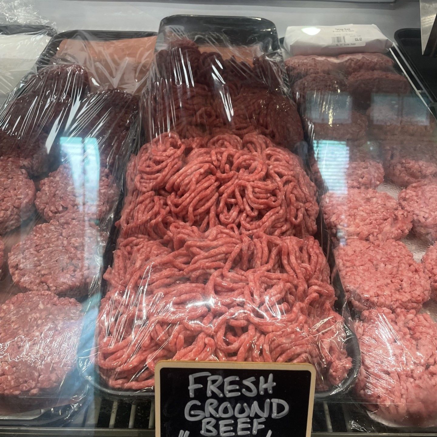 Fresh ground beef and burger patties in a display case, wrapped in plastic.