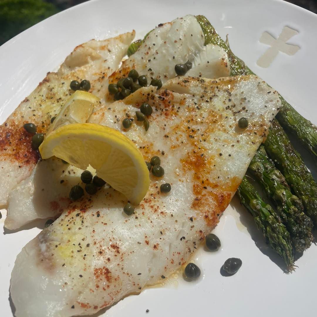 Pan-seared fish fillets with asparagus, lemon, and capers on a white plate.