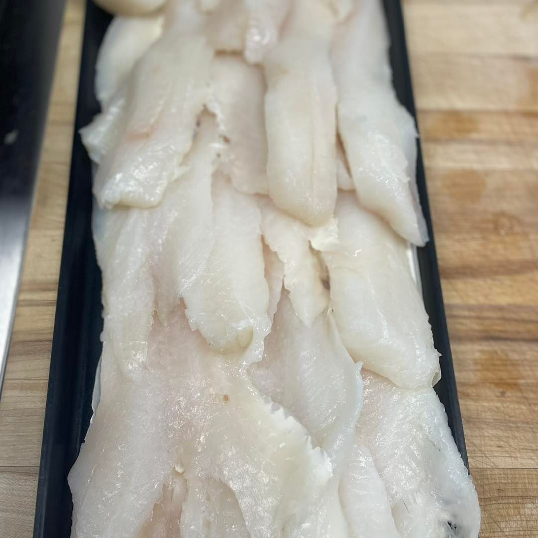 Raw, white fish fillets arranged on a black tray, ready for cooking.