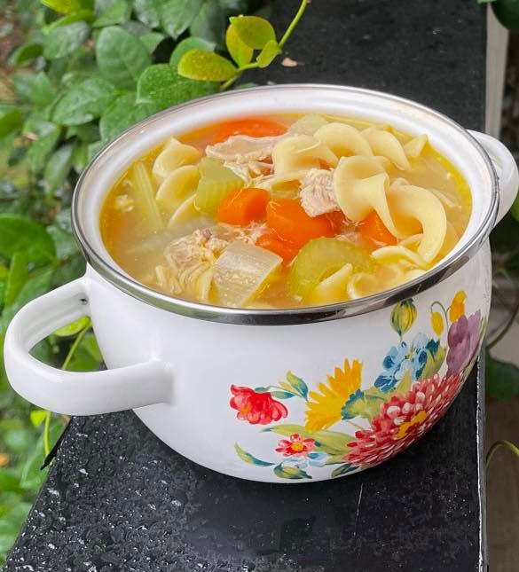 Chicken noodle soup in a floral-patterned white bowl. Carrots, celery, noodles, and chicken are visible.