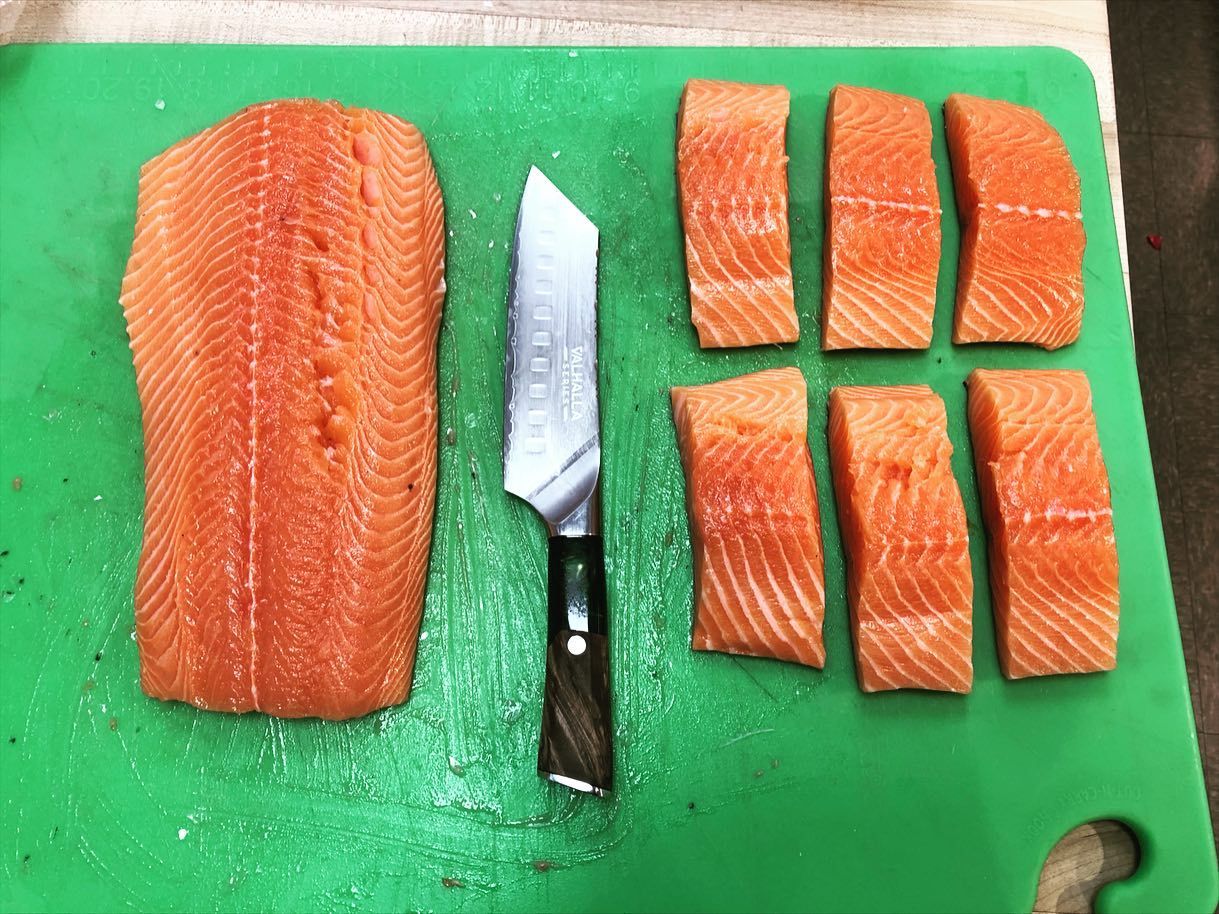 Salmon fillet and cut pieces on a green cutting board with a knife.