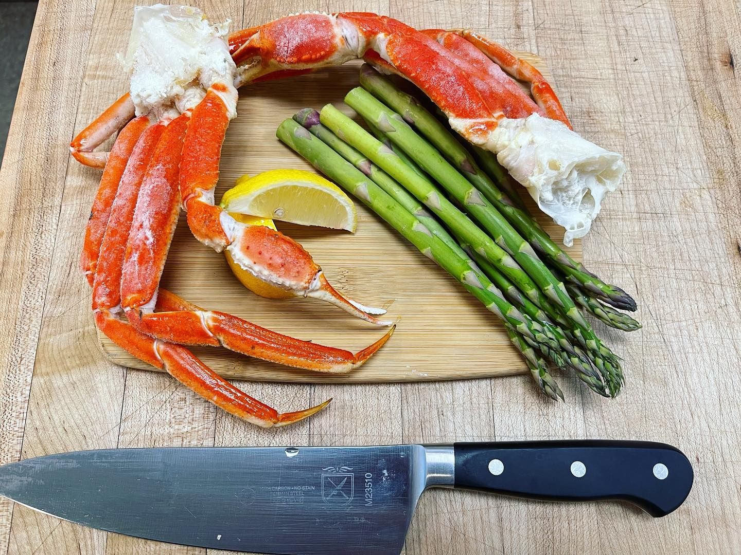 Crab legs, asparagus, lemon wedge, and chef knife on a wooden cutting board.