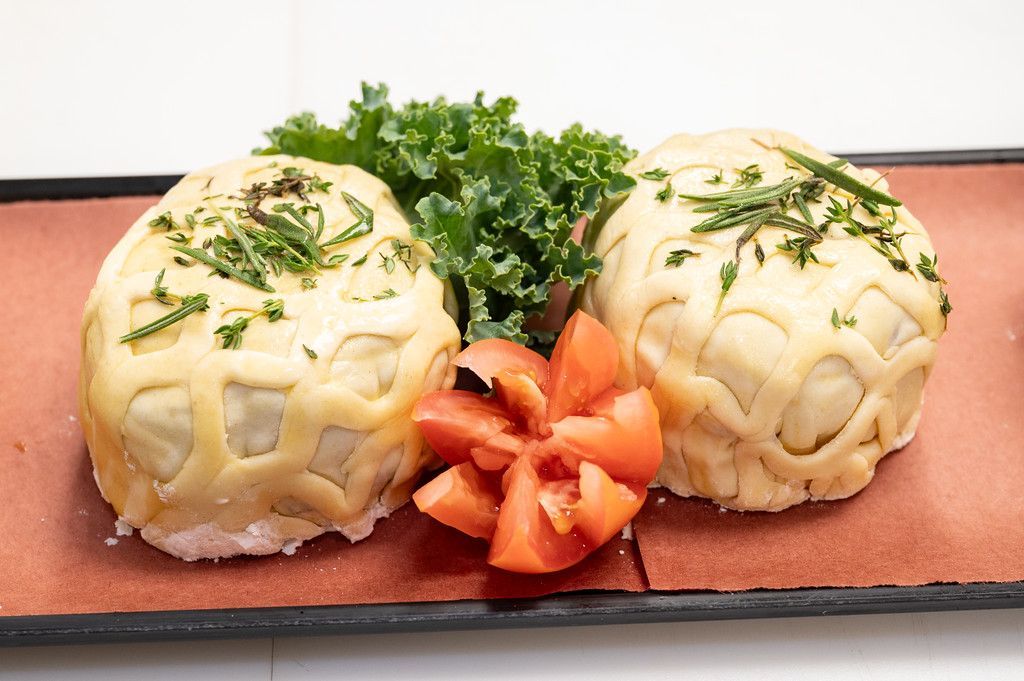 Two beige pastries with lattice crust, garnished with chives, kale, and tomato on a brown plate.