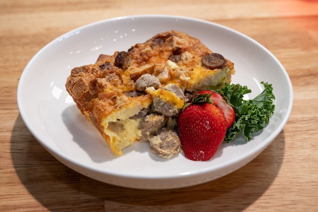 Slice of breakfast casserole with sausage, strawberry, and kale on a white plate.