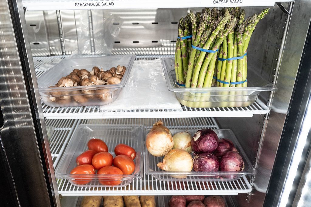 Refrigerator shelves filled with vegetables: mushrooms, asparagus, tomatoes, onions, and potatoes.