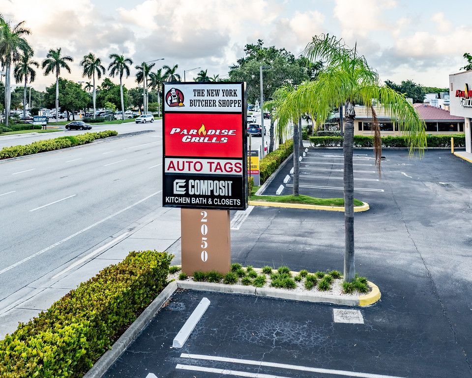 Sign with business names: The 5th Ave, Paradise Grills, Auto Tags, Compos-it. Located at 2050 with palm trees and a parking lot.