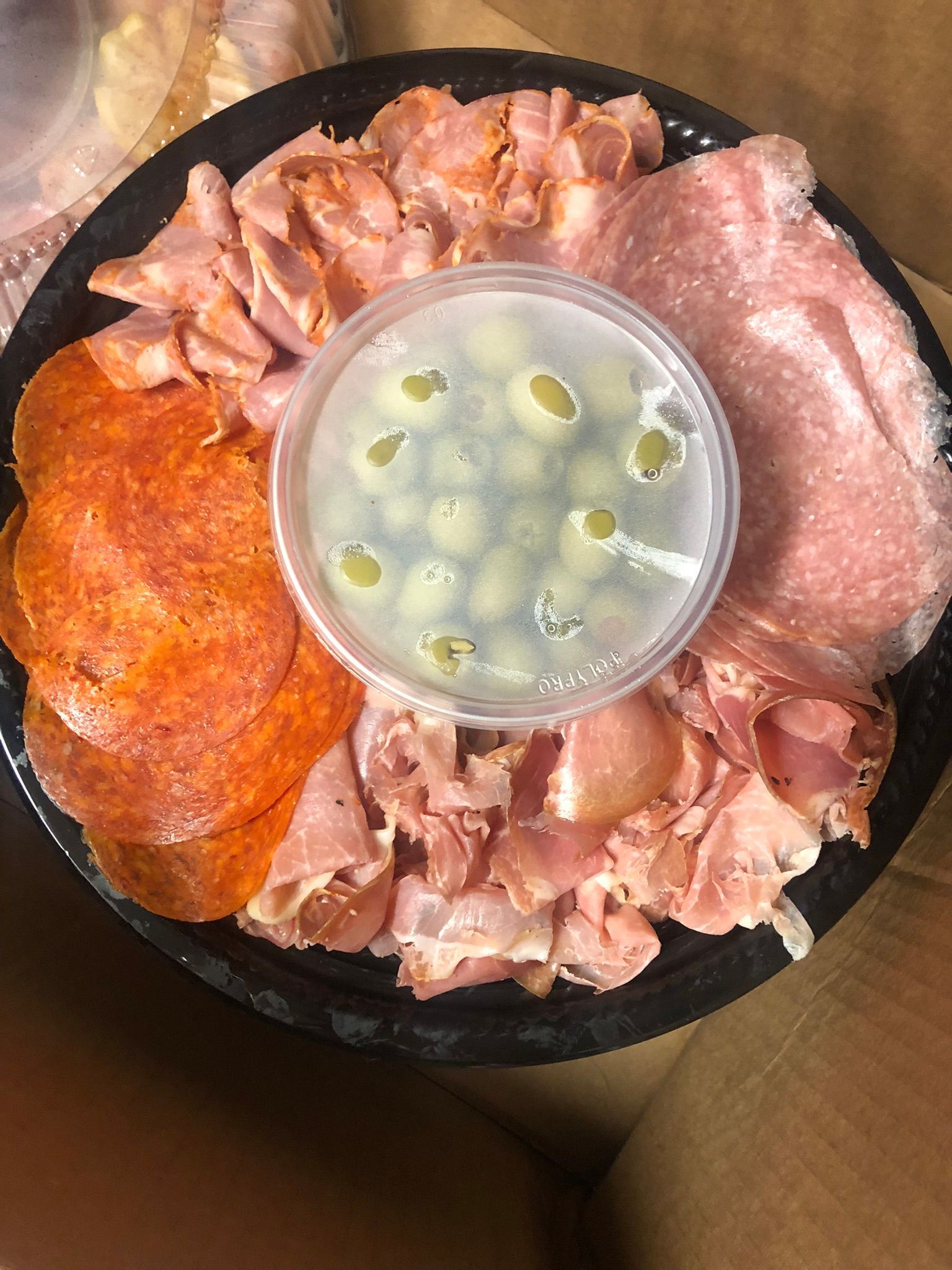 Charcuterie platter with salami, pepperoni, prosciutto, and a cup of olives.