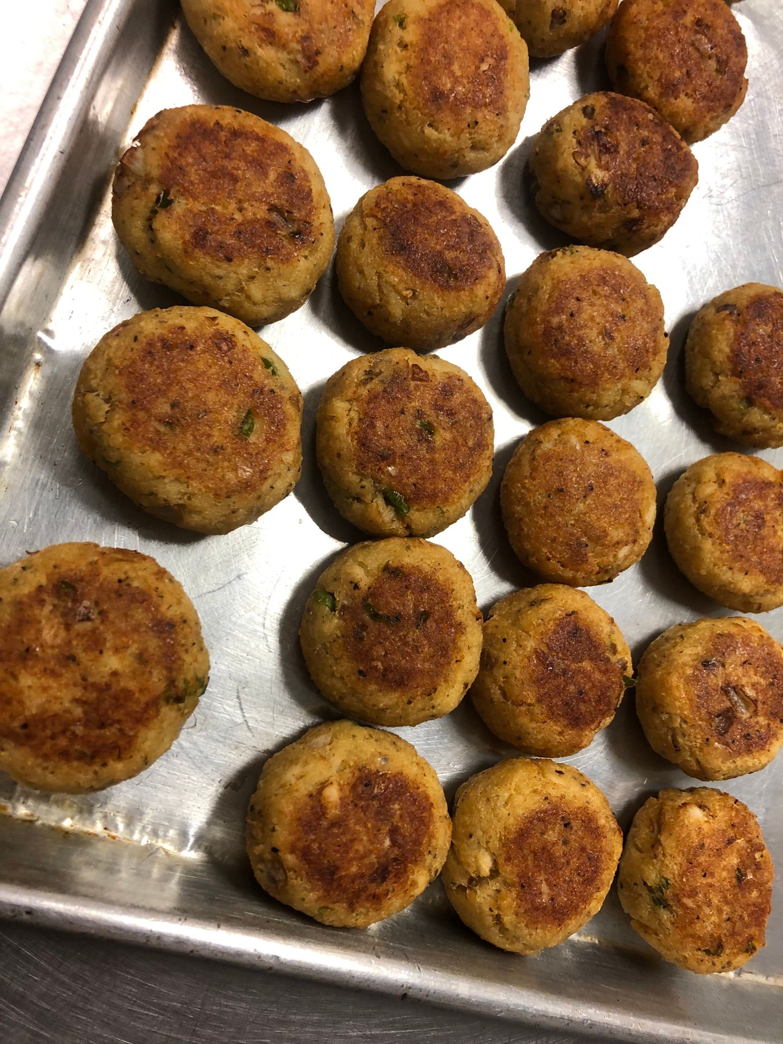 Tray of golden-brown, round, pan-fried patties; likely veggie burgers or similar dish.
