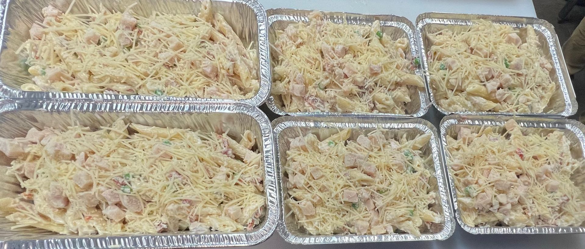 Six foil pans filled with pasta, topped with shredded cheese.