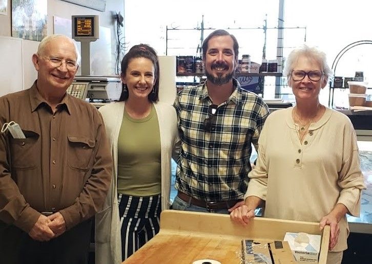 Four people pose in a store. Two women and two men, smiling. Wooden counter in the foreground.