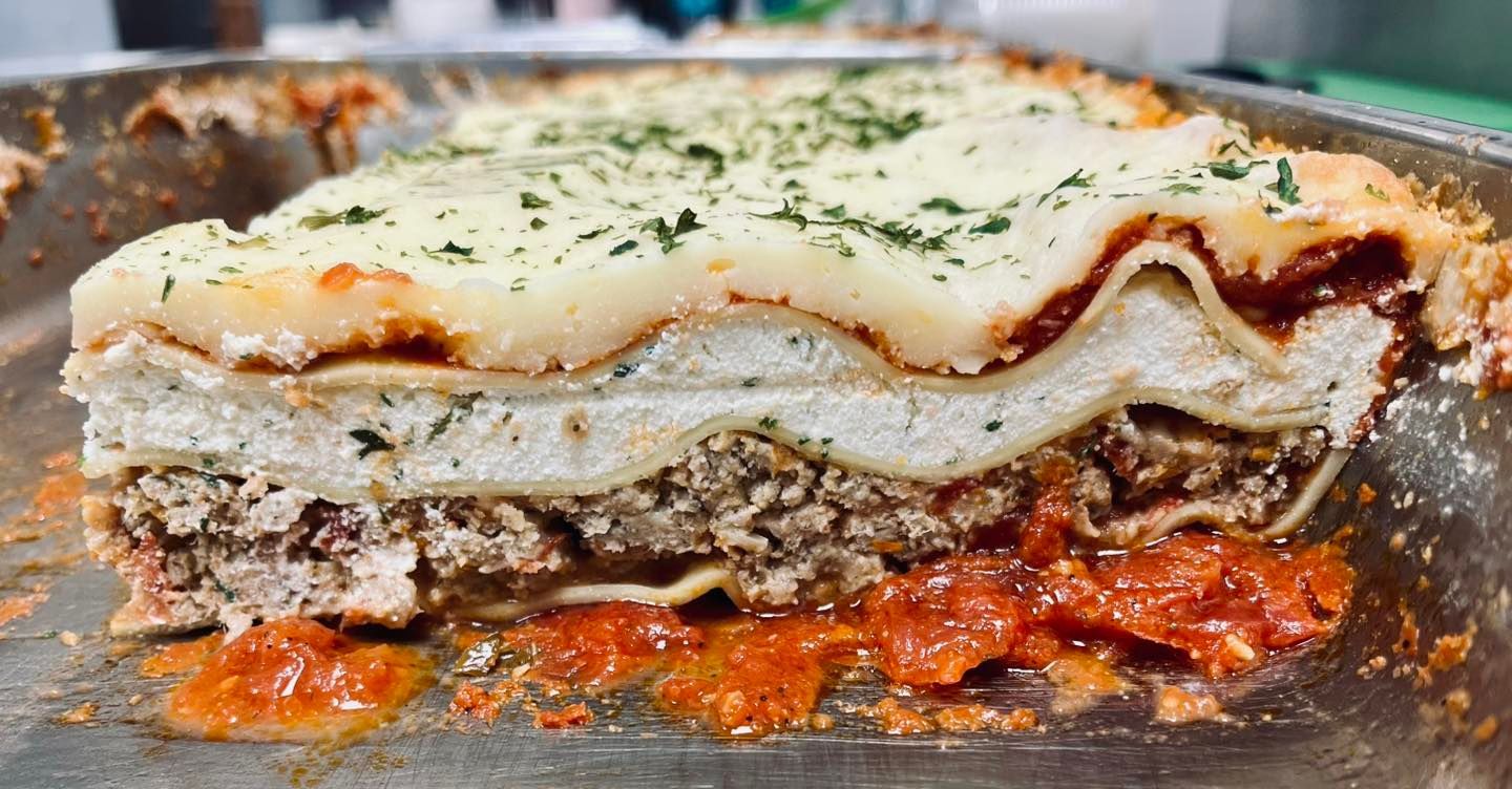 Lasagna slice, layered with meat, ricotta, tomato sauce, and mozzarella, topped with herbs.