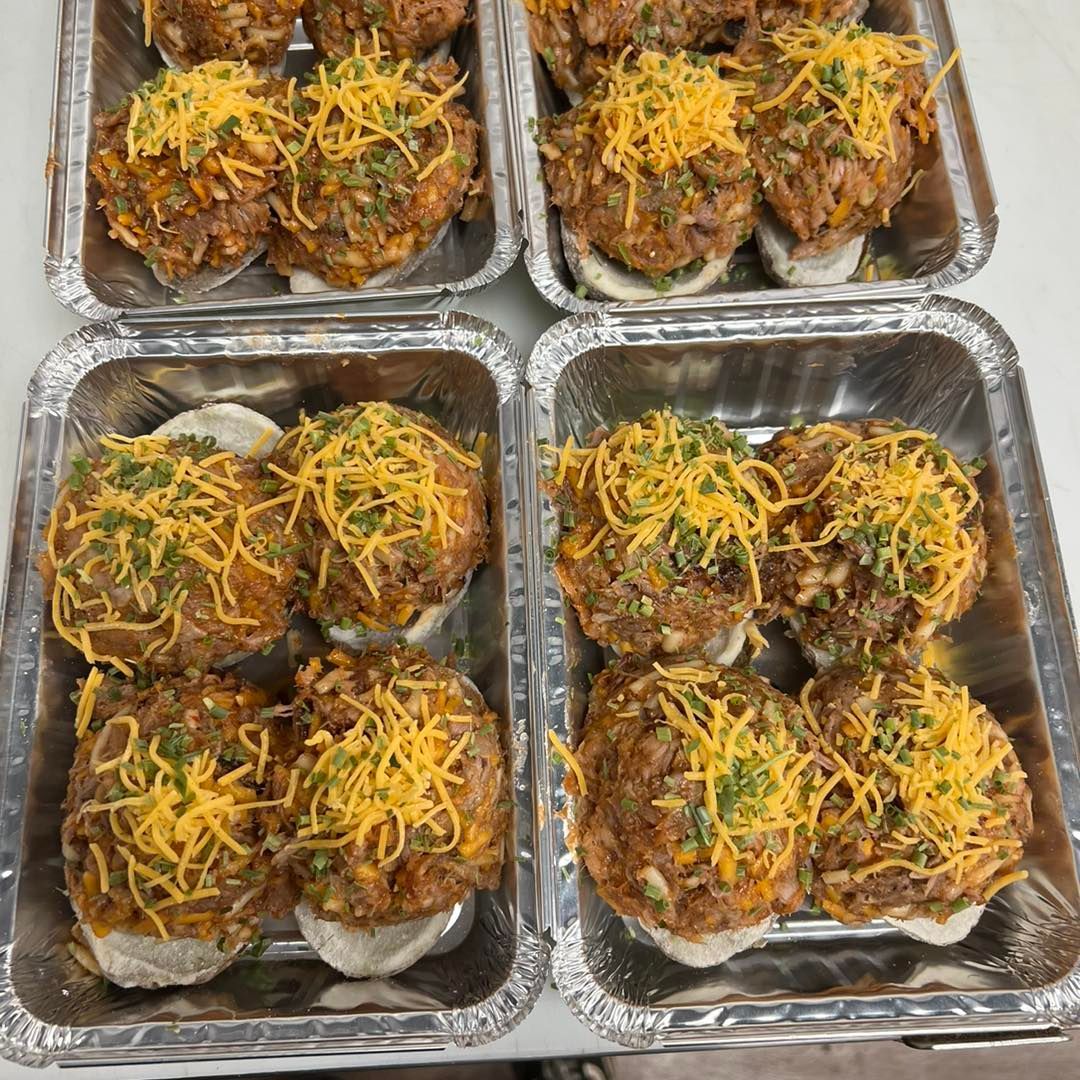 Six foil trays filled with loaded baked potatoes topped with shredded cheese and herbs.