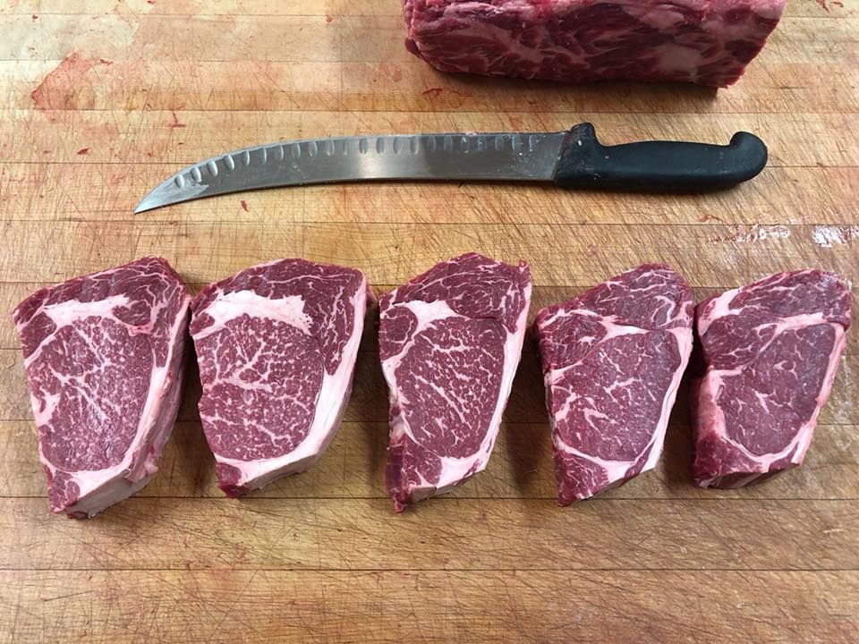Five cut ribeye steaks with knife on wooden cutting board.