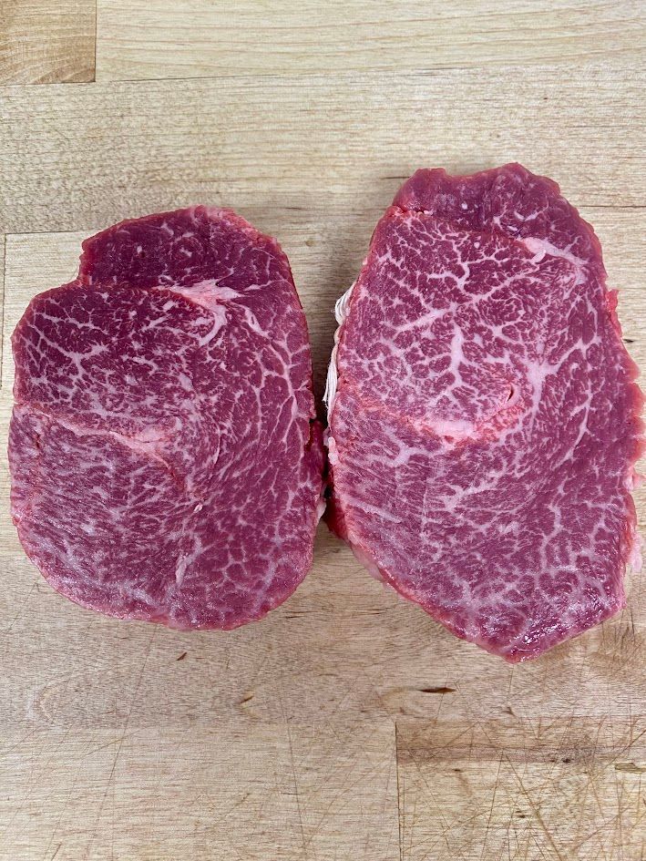 Two raw steaks with extensive marbling on a wooden surface.