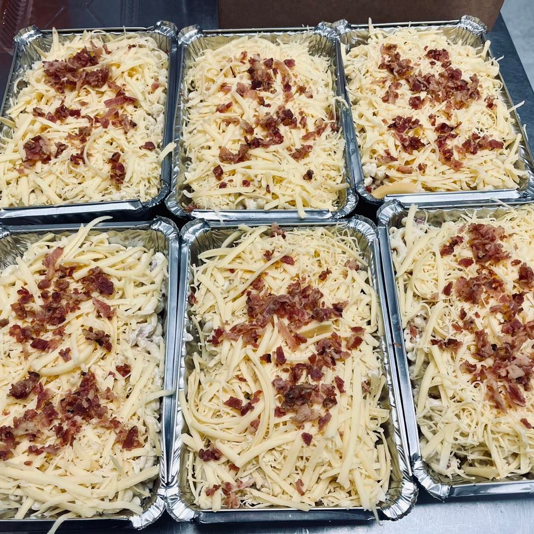 Six aluminum trays filled with cheesy pasta topped with bacon.