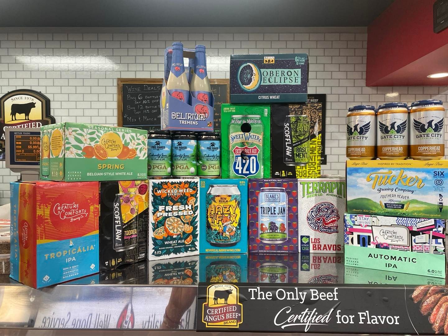 Beer display in a store, with various canned beers on a counter against a white brick wall.