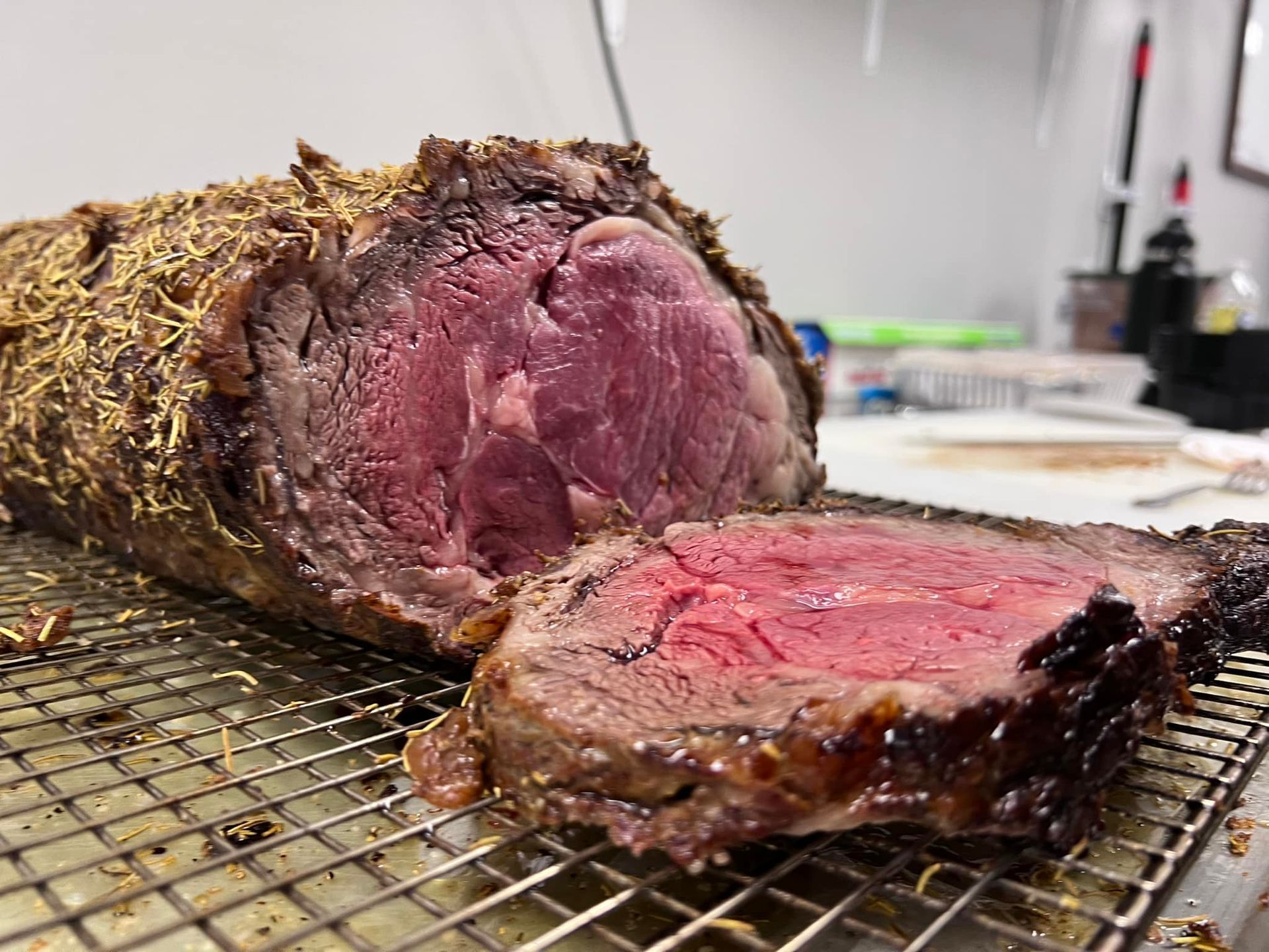 Roasted prime rib, sliced to show a red, medium-rare interior, set on a wire rack.