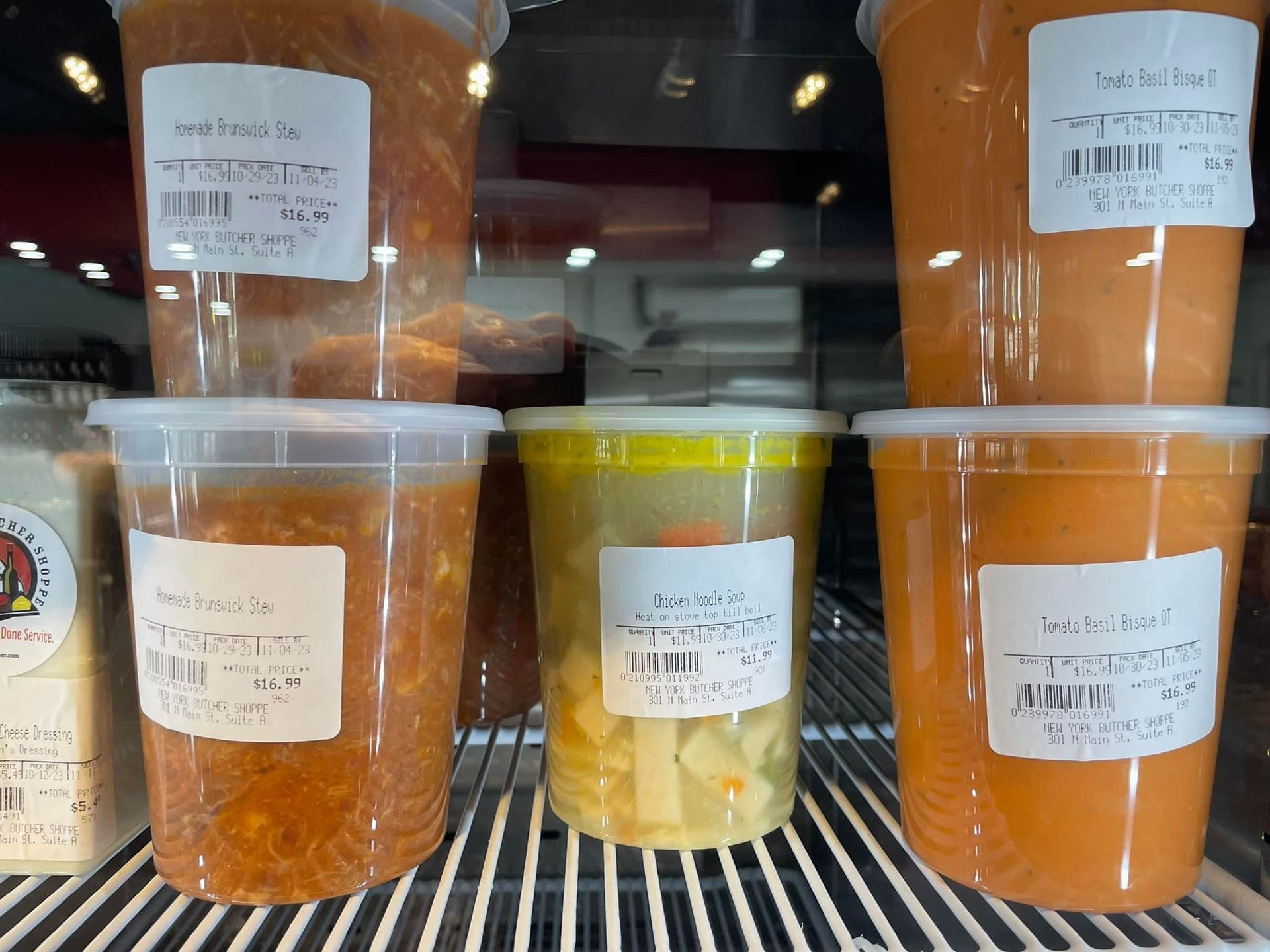 Containers of soup in a refrigerated display case; orange, yellow, and tomato colors.