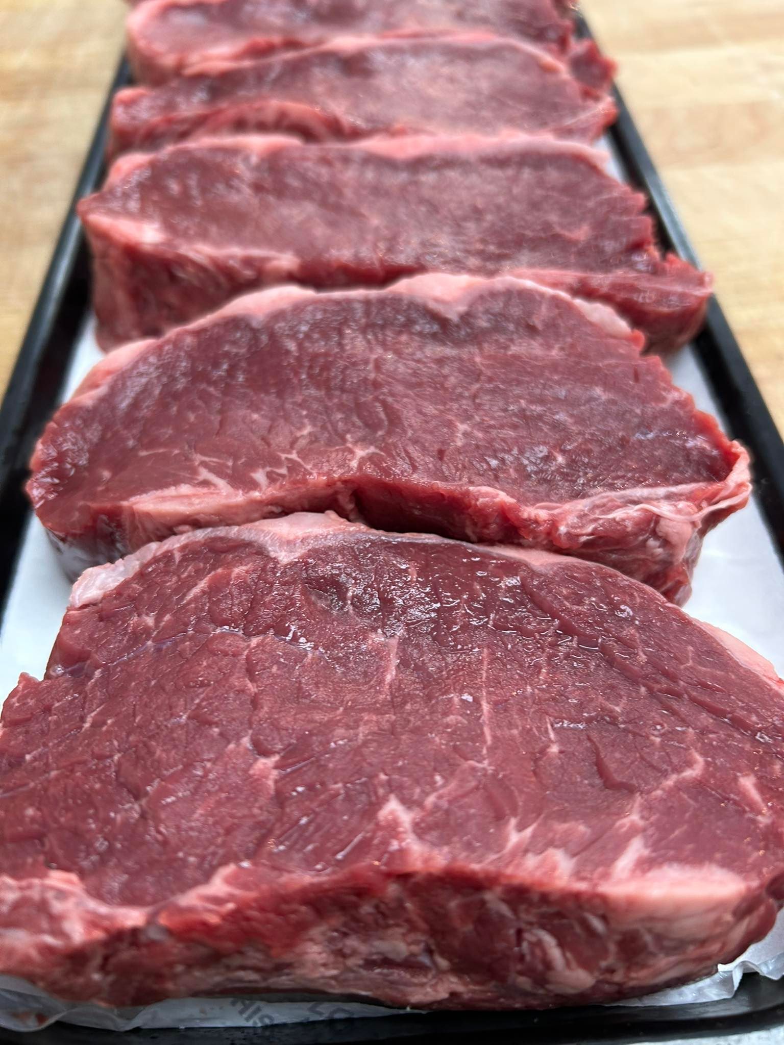 Raw steaks, seasoned with salt, arranged on a tray.