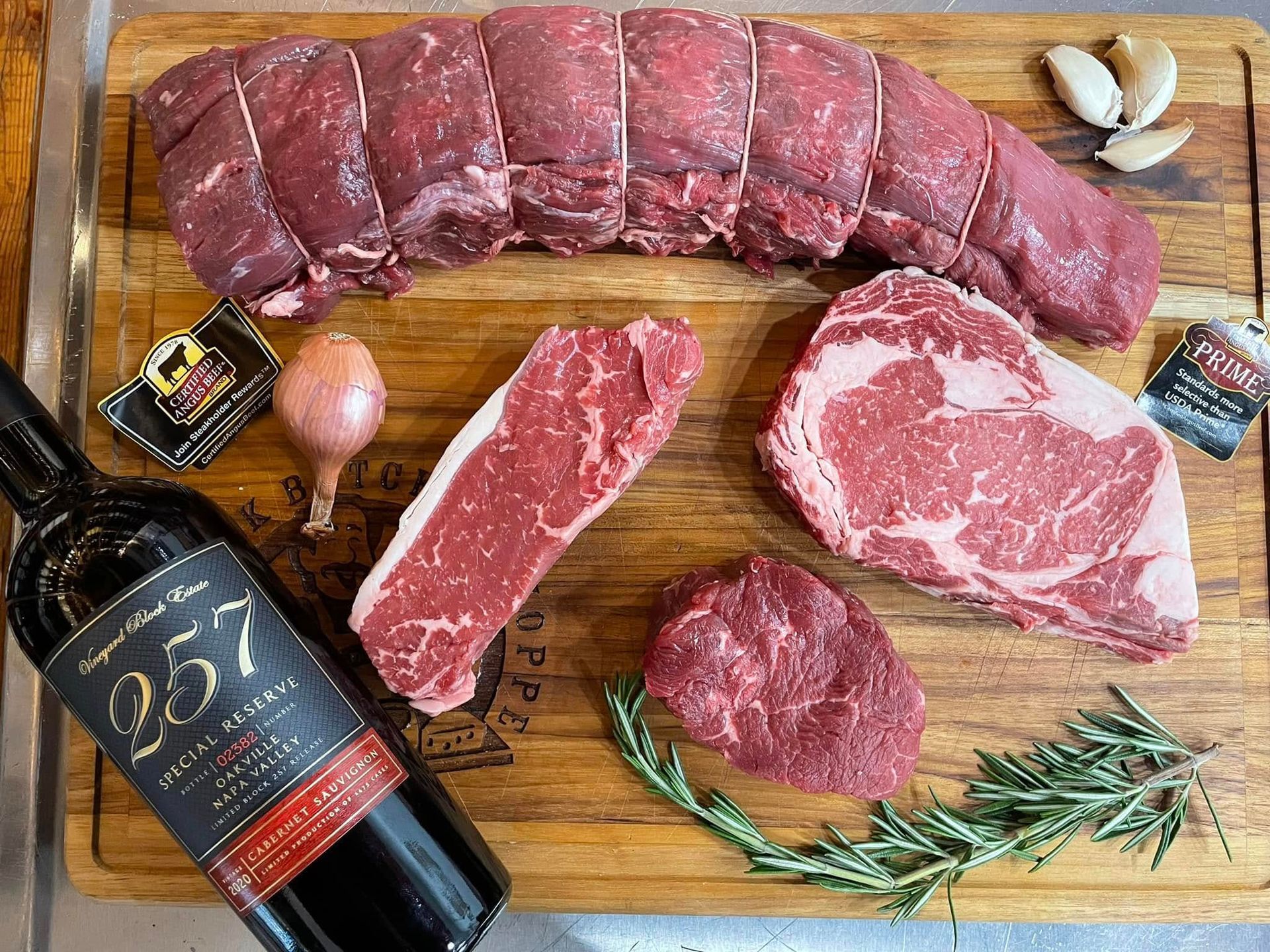 Raw cuts of meat and wine bottle on a wooden cutting board.
