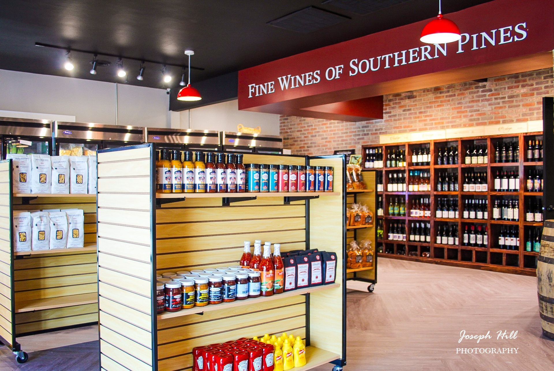 Wine shop interior with shelves of wine bottles and other products; brick wall backdrop.