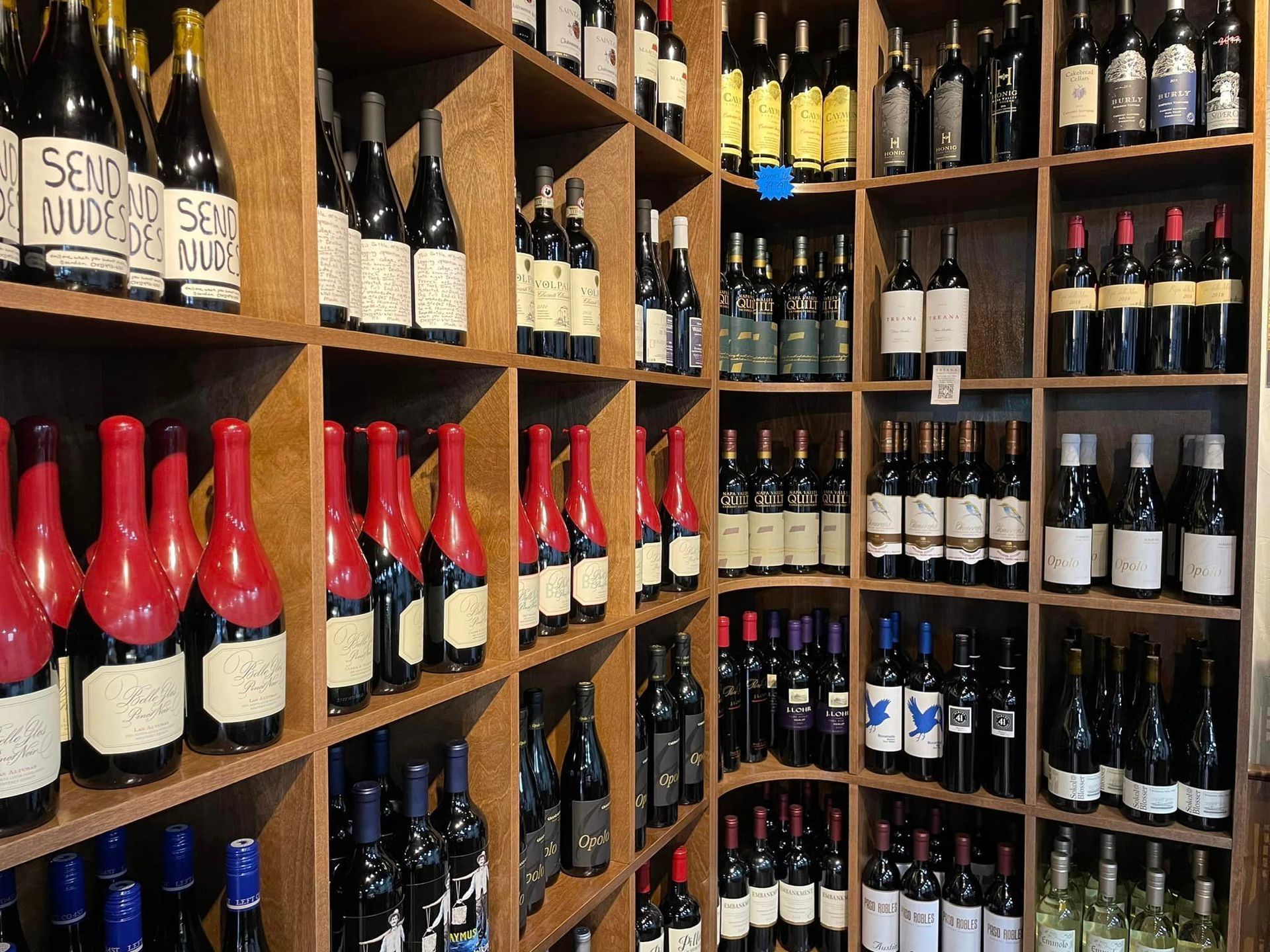 Shelves of wine bottles in a shop, various colors and sizes, wooden shelves, dimly lit.