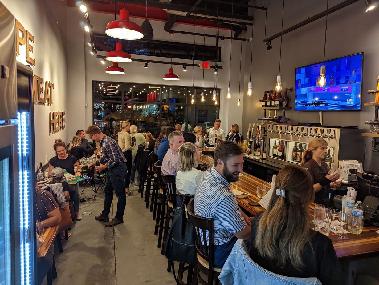 Restaurant interior: patrons at tables and bar, staff behind the bar, TV screen, red accents, soft lighting.