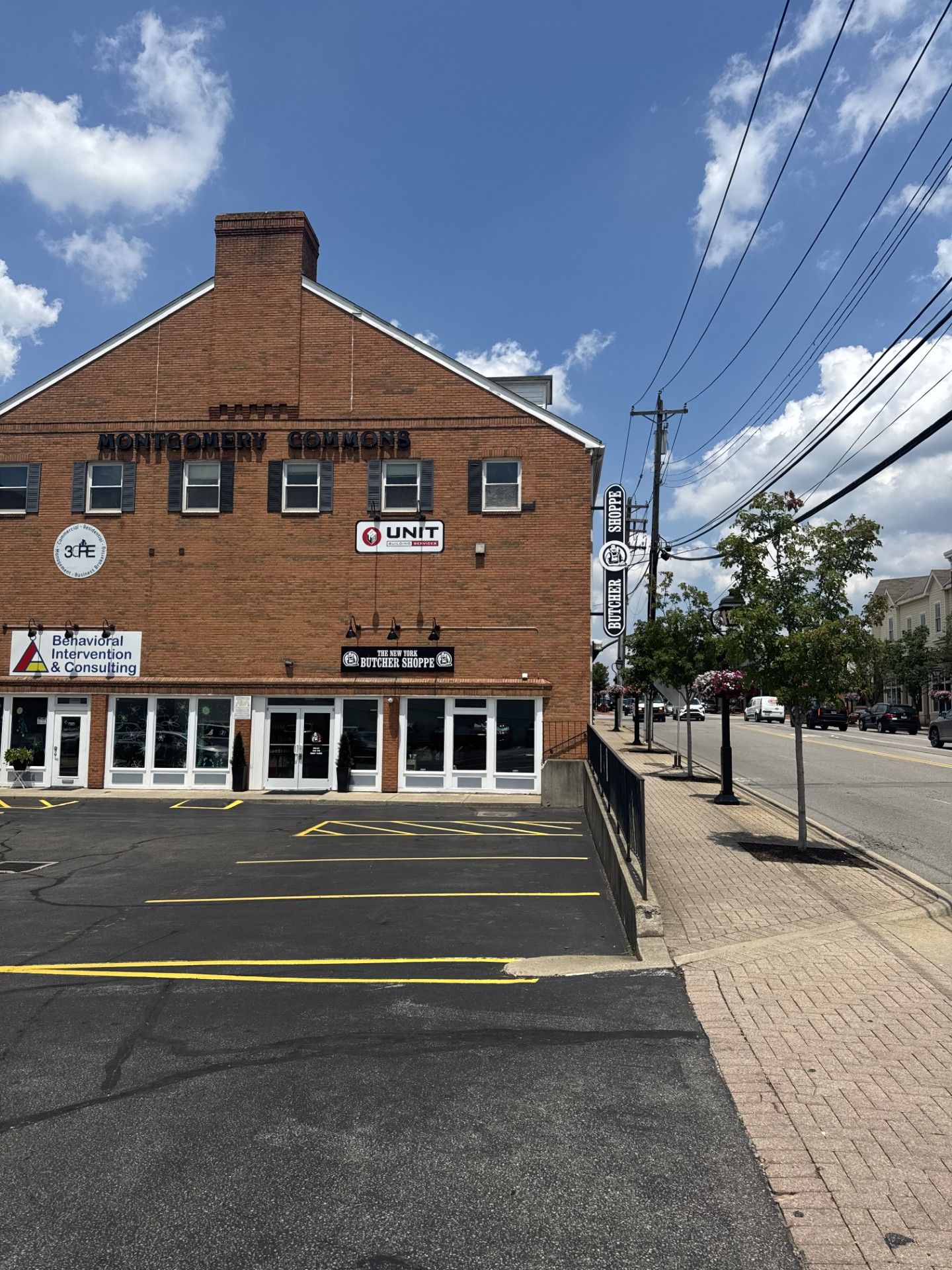 Brick building with shops, black asphalt parking, sidewalk, street, and blue sky.