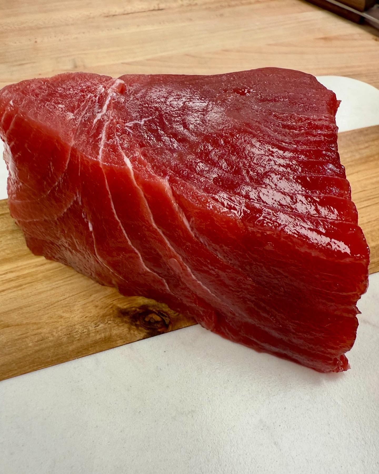 Raw, ruby-red tuna steak on a wooden cutting board, resting on a white cloth.
