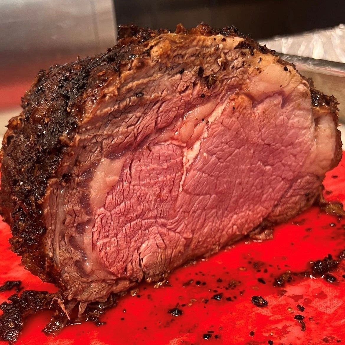 Roasted prime rib, cut to show a medium-rare interior, on a red cutting board.